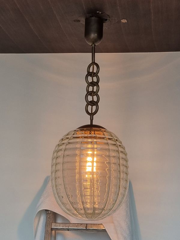 Vintage ribbed-glass pendant on a chunky chain, lit, hanging from a wooden ceiling