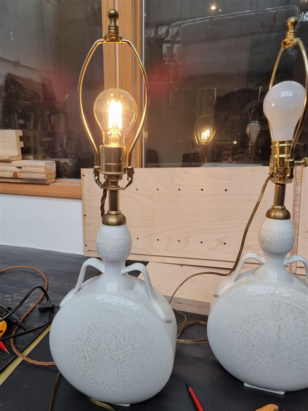 A matching pair of white porcelain lamps: the left one converted to British fittings and lit, the right one still on its original American fittings